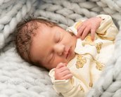 Neugeborenes Baby mit lockigem Haar, das in einem weichen, grauen Strickmaterial liegt und einen gelben Schlafanzug mit Löwenmotiven trägt.