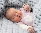 Neugeborenes Baby schläft friedlich in einer weichen, grauen Decke, trägt einen rosa Strampler mit einer Blumenapplikation.