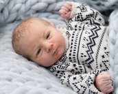 Neugeborenes Baby in einem gestrickten Pullover mit geometrischem Muster, auf einer weichen Decke liegend und in die Kamera blickend.