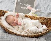 Neugeborenes Baby liegt in einem Korb, umgeben von einer Decke, mit einem Schild, das "Willkommen Amaya" zeigt, und einem Stoffhasen.