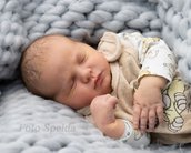 Ein schlafendes Baby liegt auf einer grauen Decke, eingekuschelt in einem weichen, beigen Outfit mit einem Muster.