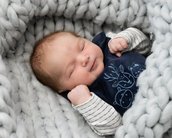 Ein schlafendes Baby in einem weichen, grauen Strickschal, trägt ein dunkelblaues Oberteil mit Tiermotiven und gestreifte Ärmel.
