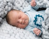 Ein schlafendes Baby in einem blauen Oberteil mit einem Löwenmotiv, eingekuschelt in eine graue, dicke Decke.