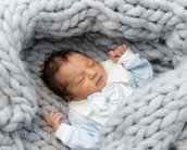Neugeborenes Baby in einem blauen Outfit mit einer großen Schleife, eingewickelt in eine graue, dicke Decke.
