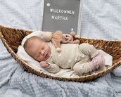 Neugeborenes Baby schläft in einem Korb, umgeben von einer Decke, mit einem Spielzeug und einem Schild, das "Willkommen Martha" zeigt.