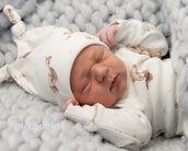 Neugeborenes Baby schläft in einem gestrickten Nest, trägt einen weißen Schlafanzug mit Tiermotiven und eine passende Mütze.