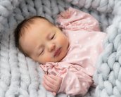 Neugeborenes Baby in einem rosa Outfit mit weißen Punkten, eingekuschelt in eine graue, gestrickte Decke.