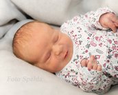 Neugeborenes Baby schläft auf einer weichen Decke, trägt einen bunten, gemusterten Schlafanzug und hat die Hände leicht geöffnet.