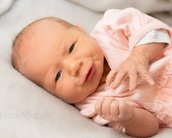 Neugeborenes Baby in einem rosa Outfit, das auf einer weichen Unterlage liegt und mit einer Hand spielt.