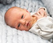 Neugeborenes Baby mit blauen Augen, das auf einer weichen Decke liegt und in die Kamera schaut. Es trägt einen hellen, einfachen Schlafanzug.
