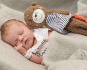 Schlafendes Baby in einer Decke, umarmt ein braunes Stofftier mit einem gestreiften Outfit.