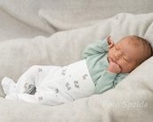 Ein schlafendes Baby in einem grauen Nest, gekleidet in einen mintgrünen Oberteil und weißen Schlafanzug mit Tiermotiven.