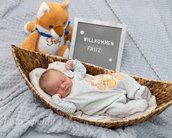 Neugeborenes Baby liegt in einem Korb, umgeben von einem Plüschfuchs und einem Schild mit der Aufschrift „Willkommen Fritz“.