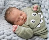 Schlafendes Baby in einem grünen, monsterförmigen Overall, eingekuschelt in eine graue, gestrickte Decke.