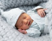 Neugeborenes Baby schläft friedlich in einer grauen Decke, trägt einen hellblauen Schlafanzug mit Punkten und eine passende Mütze.