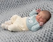 Ein schlafendes Baby in einem grauen Strickbett, trägt einen hellblauen Pullover mit einem Fuchs-Motiv und bequeme, helle Hosen.