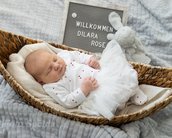 Neugeborenes Mädchen schläft in einem Korb, trägt ein weißes Kleid mit roten Punkten. Ein Schild mit "Willkommen Dilara Rose" steht daneben.
