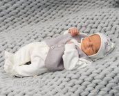 Neugeborenes Baby in einem grauen Strickoutfit mit einer hellen Mütze, das auf einer grauen Decke schläft.