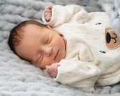 Neugeborenes Baby schläft in einem weichen, grauen Strickbett, getragen einen weißen Pullover mit Bärenmotiv.