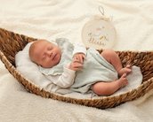 Neugeborenes Baby schläft in einem geflochtenen Korb, trägt einen hellen Anzug und hat ein Schild mit dem Namen "Elisa" daneben.
