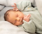 Neugeborenes Baby schläft in einer Decke, trägt einen grünen Strickpullover und hat die Hände in einer entspannten Position.