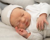 Neugeborenes Baby in einem weißen Schlafanzug und einer Mütze, das friedlich auf einer grauen Decke schläft.
