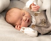 Ein schlafendes Baby in einem grauen Strampler mit Knöpfen, eingekuschelt in eine weiche Decke.