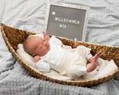 Neugeborenes Baby in einem Korb, umgeben von einer Decke, mit einem Schild, das "Willkommen Mia" zeigt.