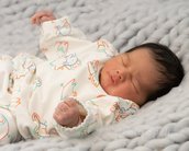 Ein schlafendes Baby in einem bunten, bedruckten Schlafanzug liegt auf einer grauen, gestrickten Decke.