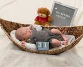Ein schlafendes Baby in einem Korb, umgeben von einem Plüschtier und einem Schild mit der Aufschrift "Willkommen Ansgar" und dem Datum "31. August".