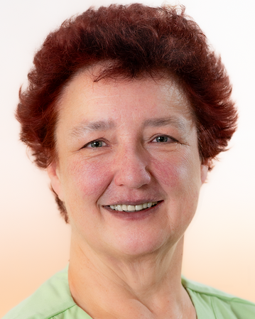 Eine lächelnde Frau mit roten Haaren trägt ein grünes Pflegehemd und hat ein Namensschild an ihrer Kleidung.