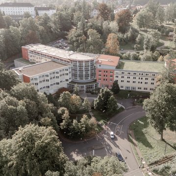 Ein modernes Gebäude umgeben von Bäumen und Grünflächen, mit einem runden Glasbereich und mehreren Etagen.