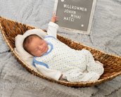 Neugeborenes Baby in einem geflochtenen Korb, trägt einen weißen Schlafanzug mit blauen Punkten. Ein Schild mit "Willkommen Joahn Mihai Matei" steht daneben.