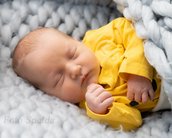 Schlafendes Baby in einem gelben Oberteil, eingekuschelt in eine graue, gestrickte Decke.