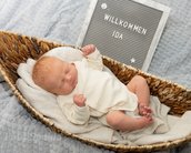 Neugeborenes Baby mit rotem Haar liegt in einem Korb, umgeben von einer Decke. Ein Schild mit der Aufschrift "Willkommen Ida" steht daneben.