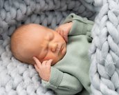 Neugeborenes Baby mit geschlossenem Gesichtsausdruck, das in einer grauen Decke liegt und die Hände an den Kopf legt.