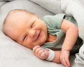 Neugeborenes Baby mit einem Lächeln, in einer Decke eingewickelt, trägt ein Armband.