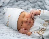 Neugeborenes Baby schläft friedlich in einem weißen Outfit mit der Aufschrift "Born in 2026" und einer passenden Mütze.