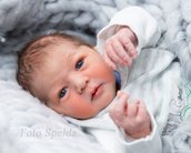 Neugeborenes Baby mit blauen Augen und hellem Haar, das auf einer weichen Decke liegt und die Hände hebt.