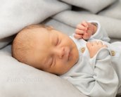 Neugeborenes Baby schläft friedlich auf einer grauen Decke, trägt einen hellen, gestreiften Schlafanzug mit Knöpfen.