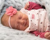 Schlafendes Baby mit blonden Haaren, rosa Blütenhaarreif und rosa Kleidung, eingekuschelt in eine weiche Decke.