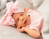 Neugeborenes Baby mit einem großen, gepunkteten rosa Haarband, das auf einer grauen Decke schläft.