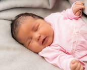 Neugeborenes Baby in rosa Kleidung schläft friedlich auf einer grauen Decke.