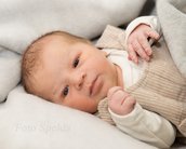Neugeborenes Baby mit hellen Augen, das in einer Decke liegt und einen beigen Strampler trägt.