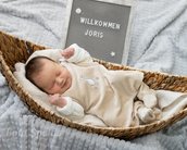 Ein schlafendes Baby in einem Korb, umgeben von einer Decke, mit einem Schild, das "Willkommen Joris" zeigt.