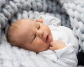 Ein Neugeborenes liegt entspannt in einer weichen, grauen Decke und schaut neugierig zur Seite.