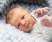 Neugeborenes Baby mit blauen Augen, das auf einer weichen, grauen Decke liegt und die Hände leicht bewegt.