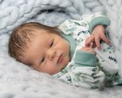 Neugeborenes Baby in einem gestreiften, blauen Strampler mit Pflanzenmuster, auf einer weichen, hellen Decke liegend.