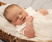 Neugeborenes Baby schläft friedlich in einem Korb, eingekleidet in ein weißes Kleidchen, mit einer Hand an der Brust.