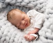 Ein schlafendes Neugeborenes in einem weißen Oberteil, eingekuschelt in eine graue, dicke Decke.